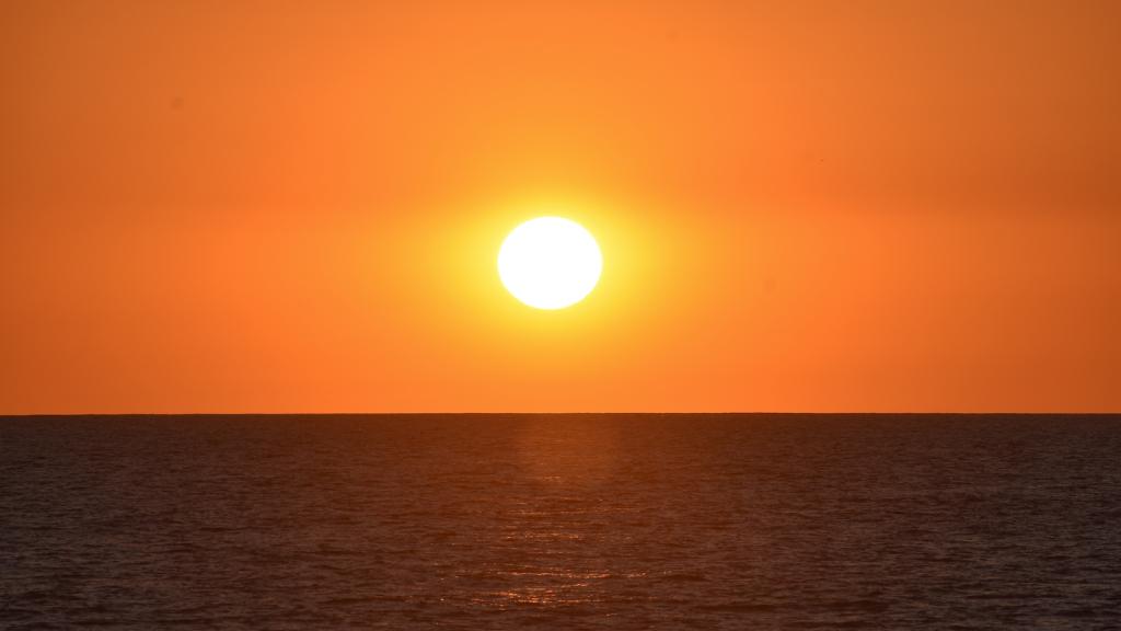 the sun hovers low in the horizon over the ocean. The sky is orange.