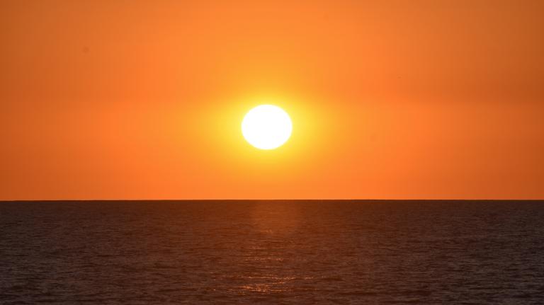 the sun hovers low in the horizon over the ocean. The sky is orange.