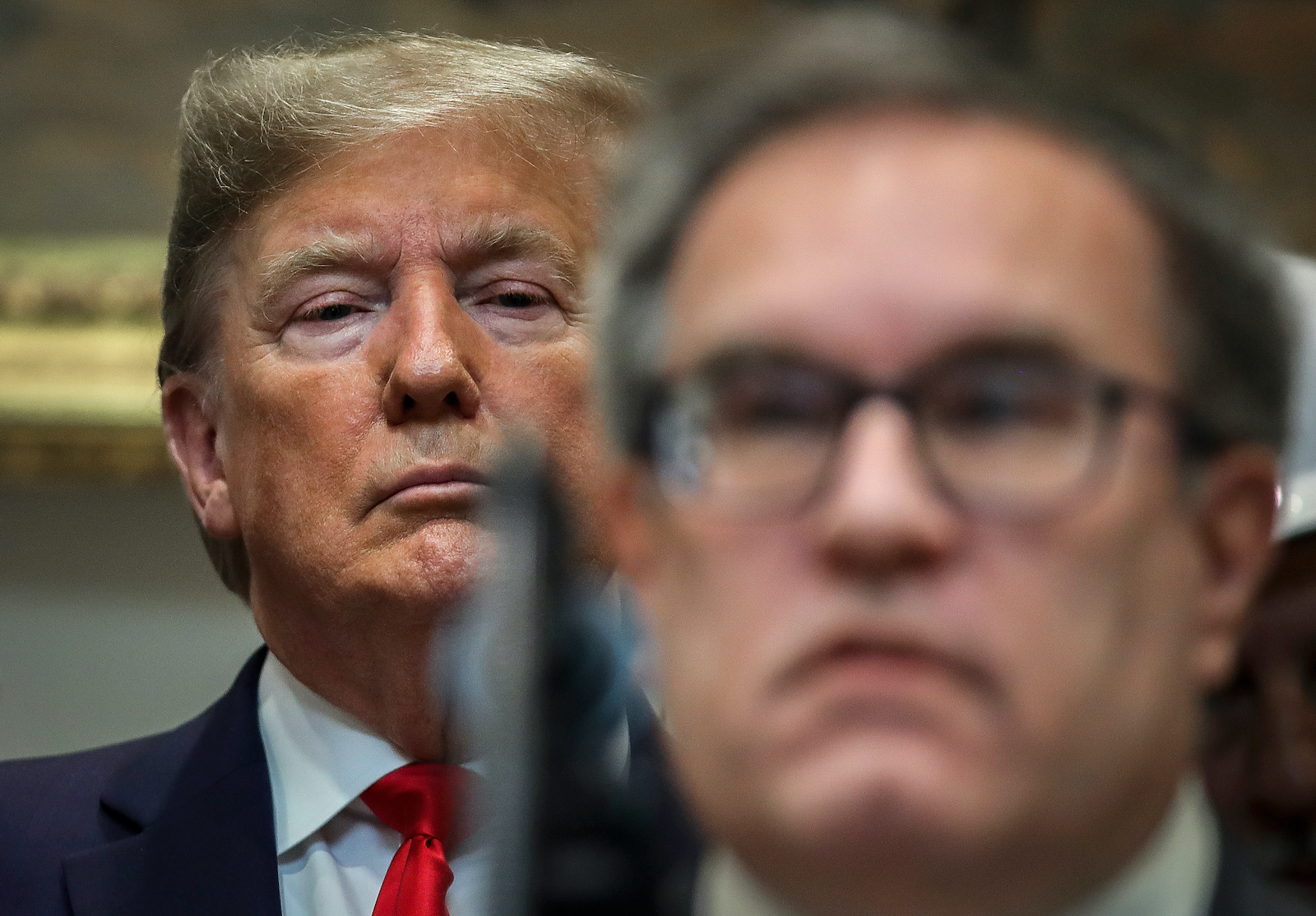 President Trump wears a red tie and suit and sits directly behind Andrew wheeler, seen wearing glasses