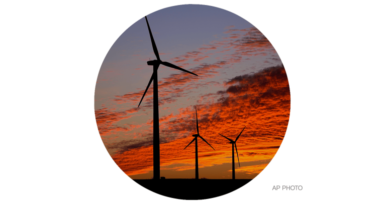 Wind turbines are silhouetted against the sky at sunset