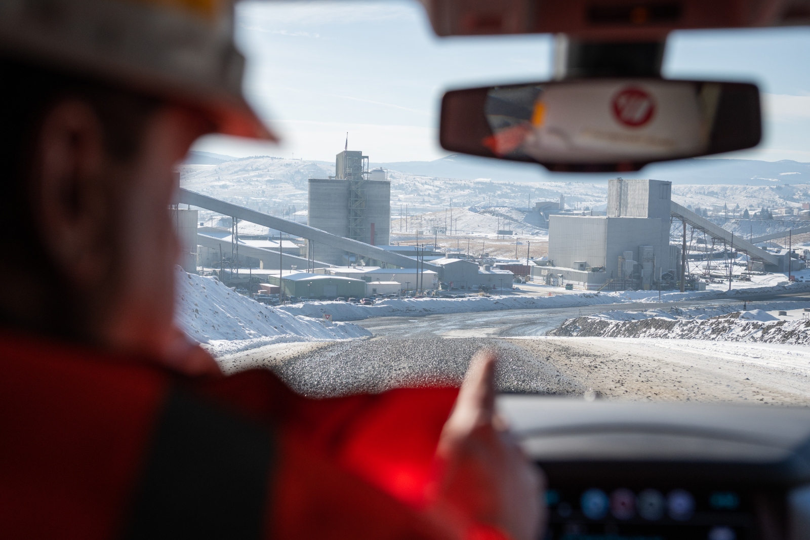 A man in a hard hat drives his car, and there's a view of a mine from his windshield.