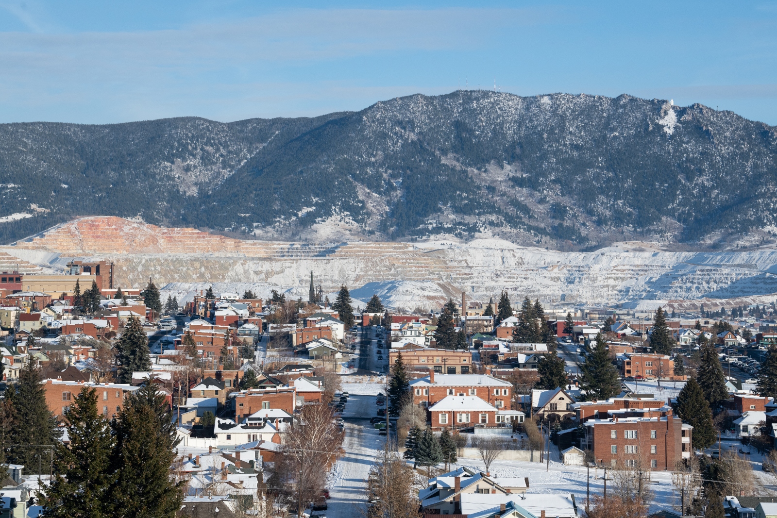 An aerial view of a snow-covered Montana town in the foothills of a mountain, with a mine scraped out in the foothills of the mountain