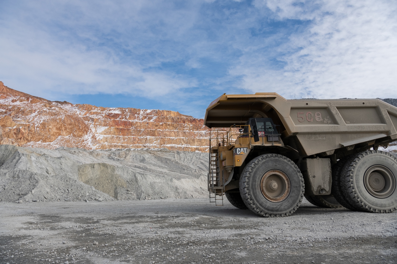 A close-up of a dump truck parked in front of a red and gray mine on the side of a mountain.