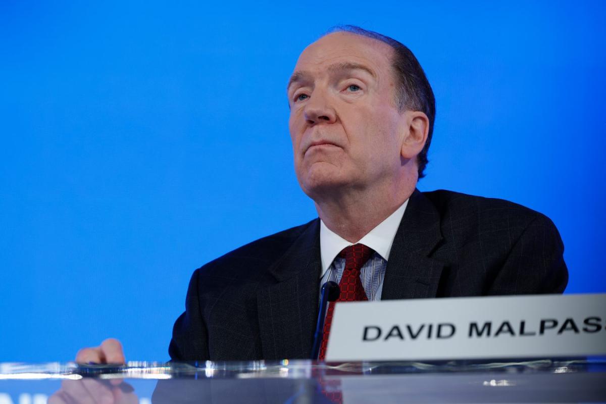 An older man in a dark suit sits at a podium with his name plaque saying "David Malpass"