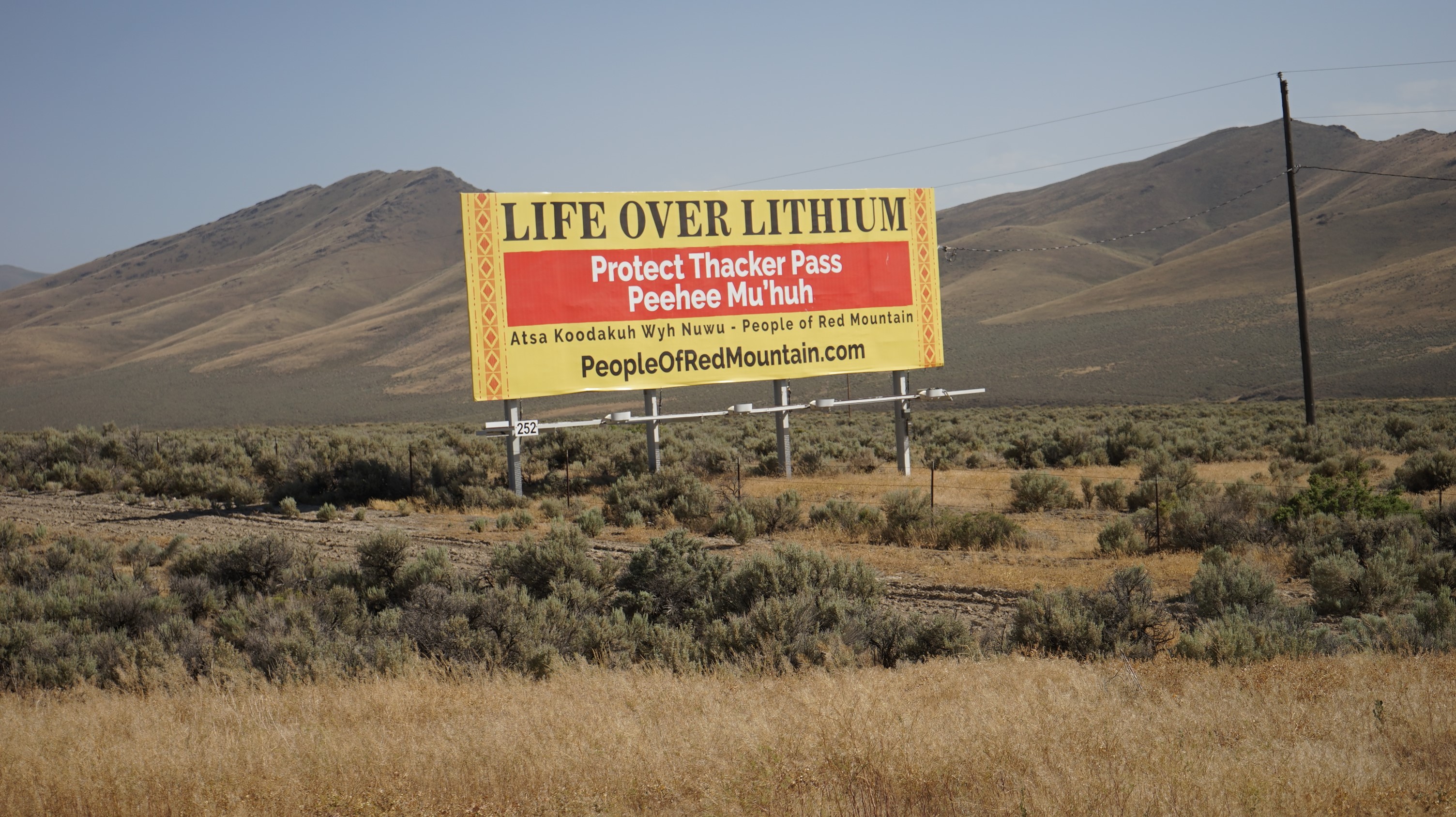 a sign reads "life over lithium" with mountains in the background