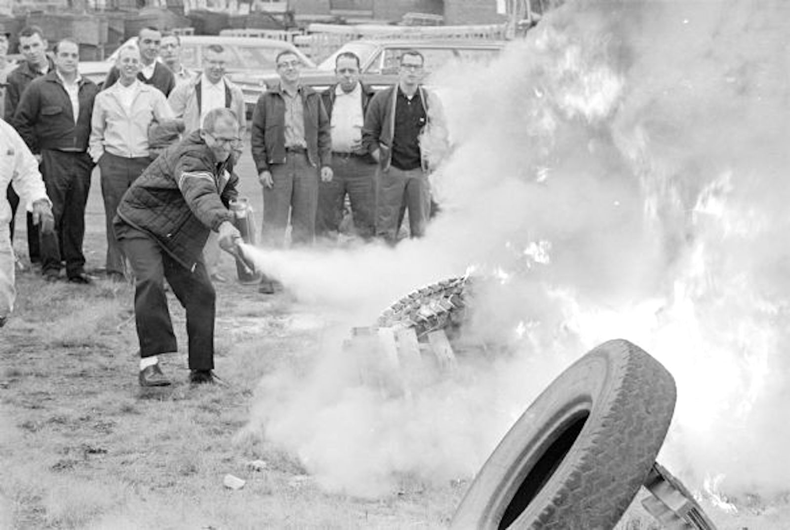 a black and white photo of a man in a suit blasting white foam over a tire