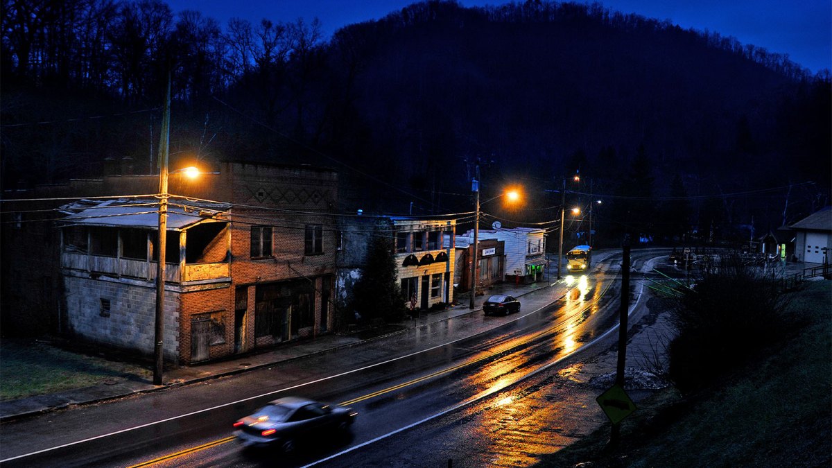 The town of Kimball, West Virginia, at dawn; a car drives down a street lit by streetlights past a handful of buildings