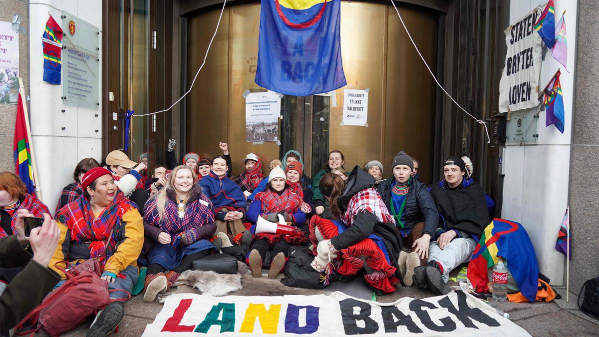 group of climate activists in front of building with protest signs reading "land back"
