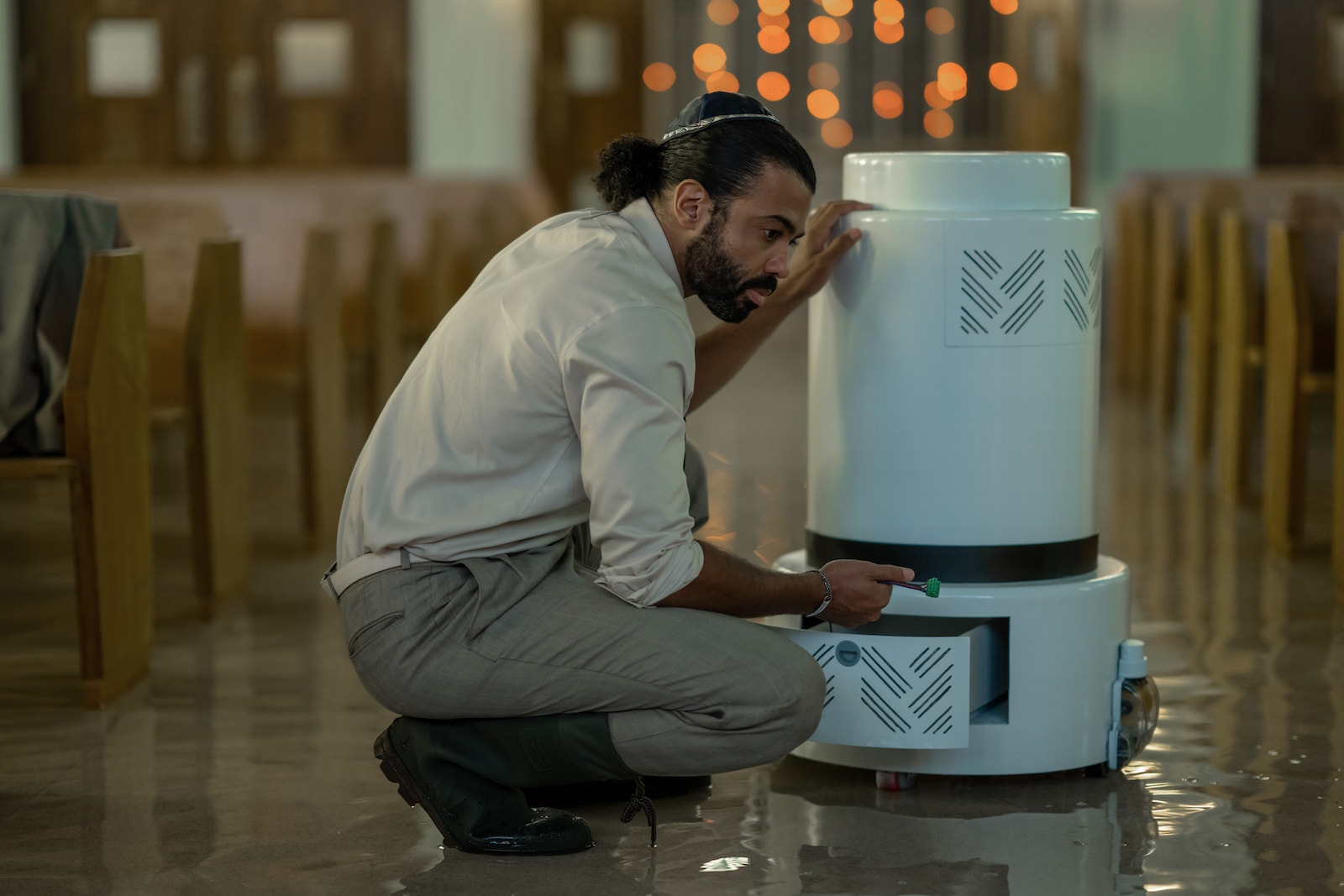 a man in a white shirt and khakis kneels near a robot