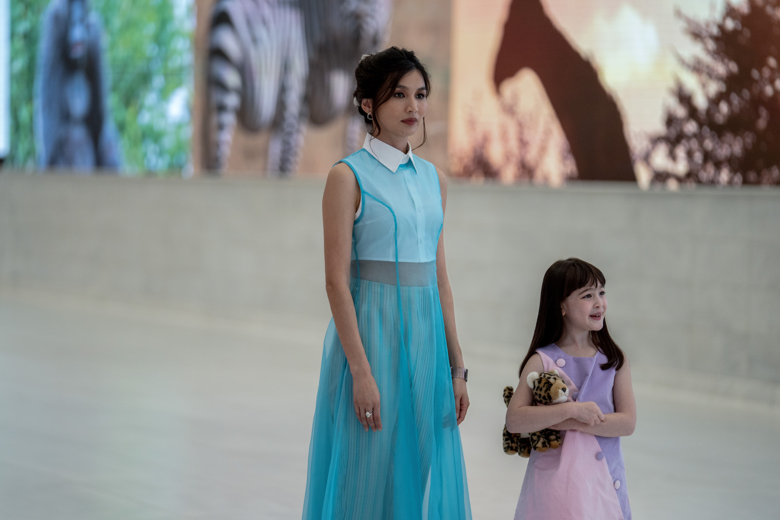 a woman in a blue dress standing with a young girl holding a stuffed animal
