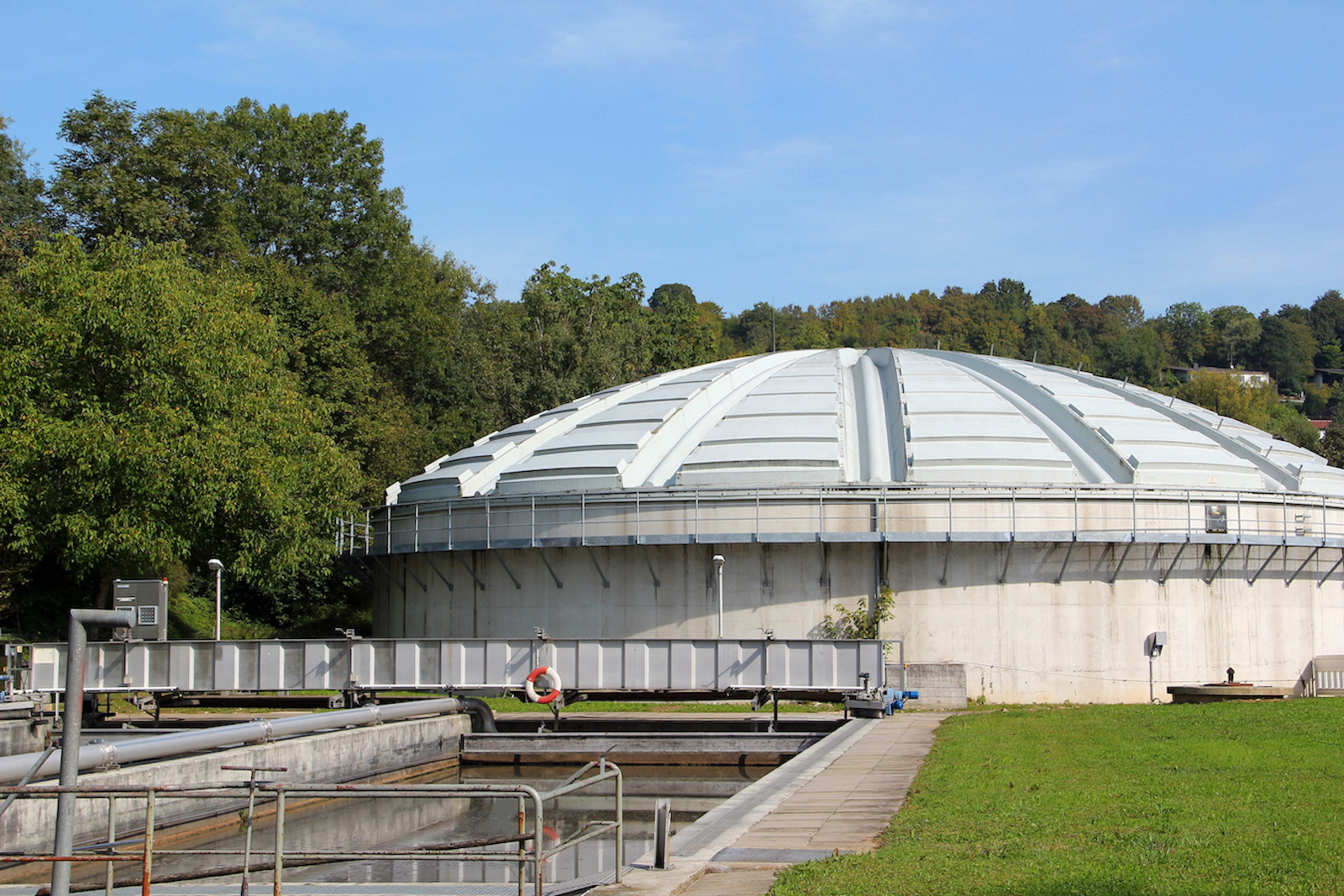 A wastewater treatment plant which consists of a domed building next to a rectangular pool of water.