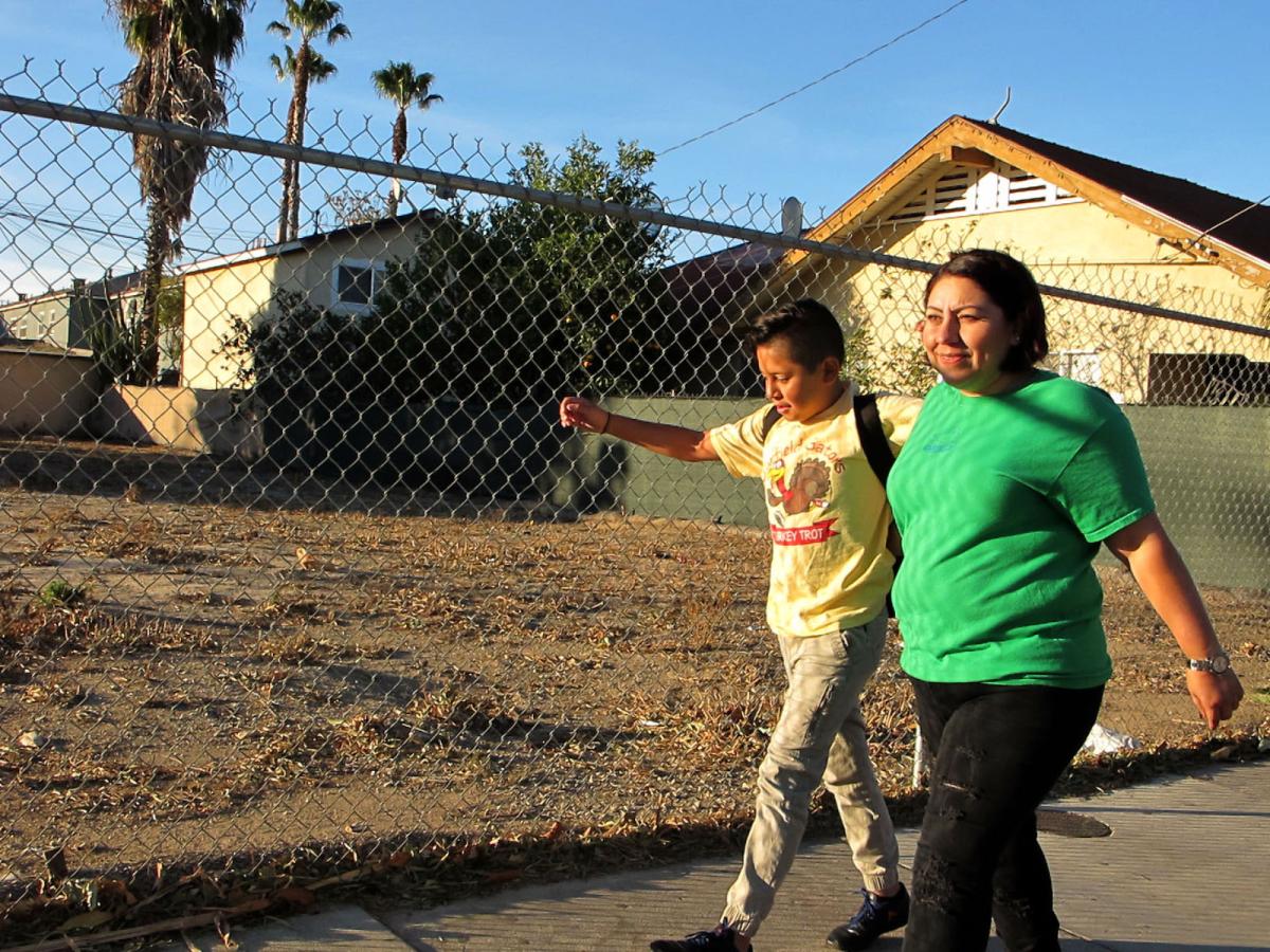 Photo of a Santa Ana parent walking her son to school near a vacant dirt lot