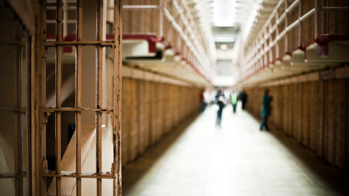 A view down a prison corridor, showing bars and cell doors.