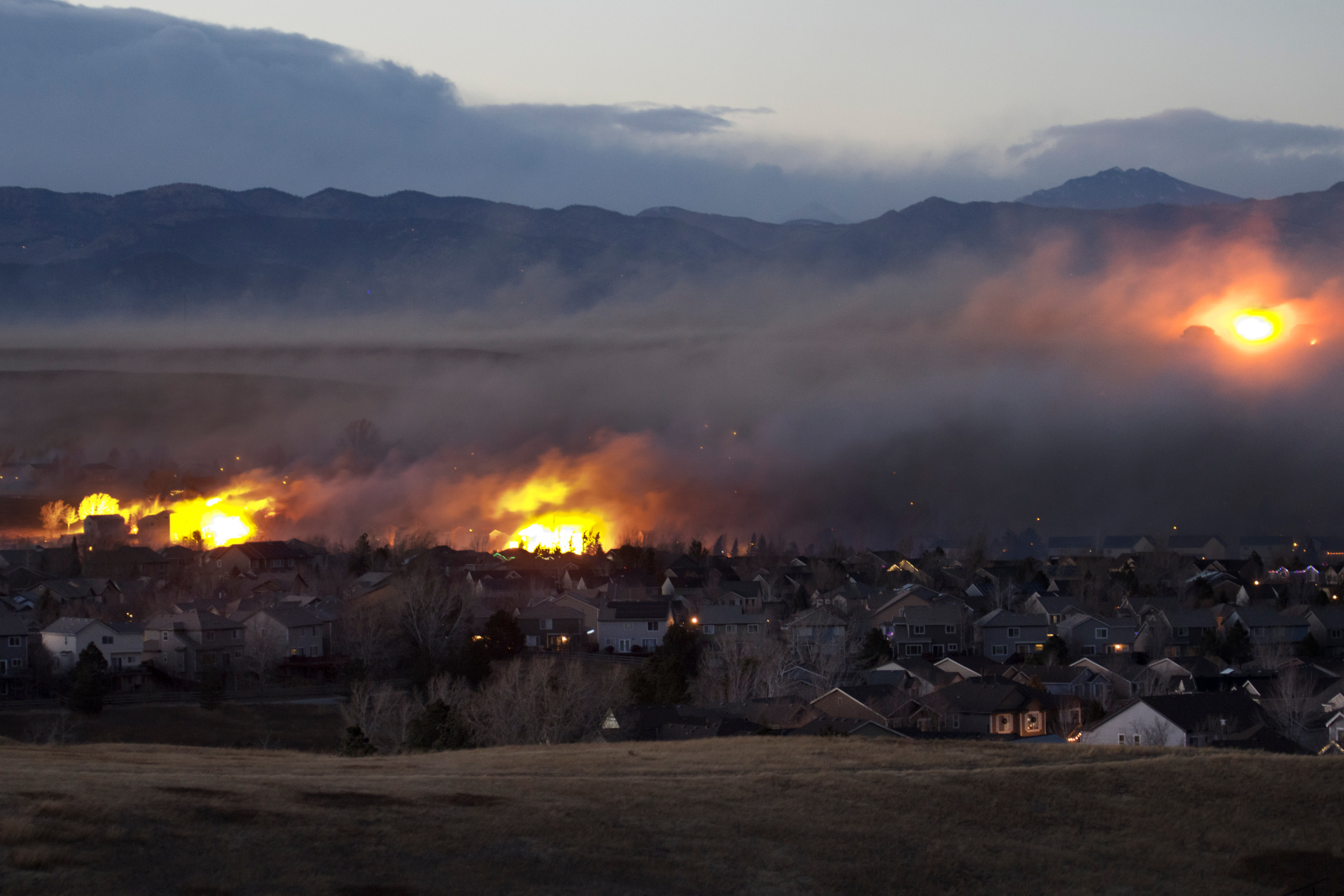 Photo of fires burning in the brush behind homes in a mountainous area