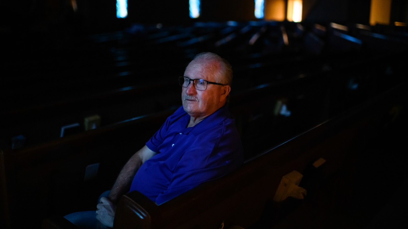 a man in glasses sits in a dark room