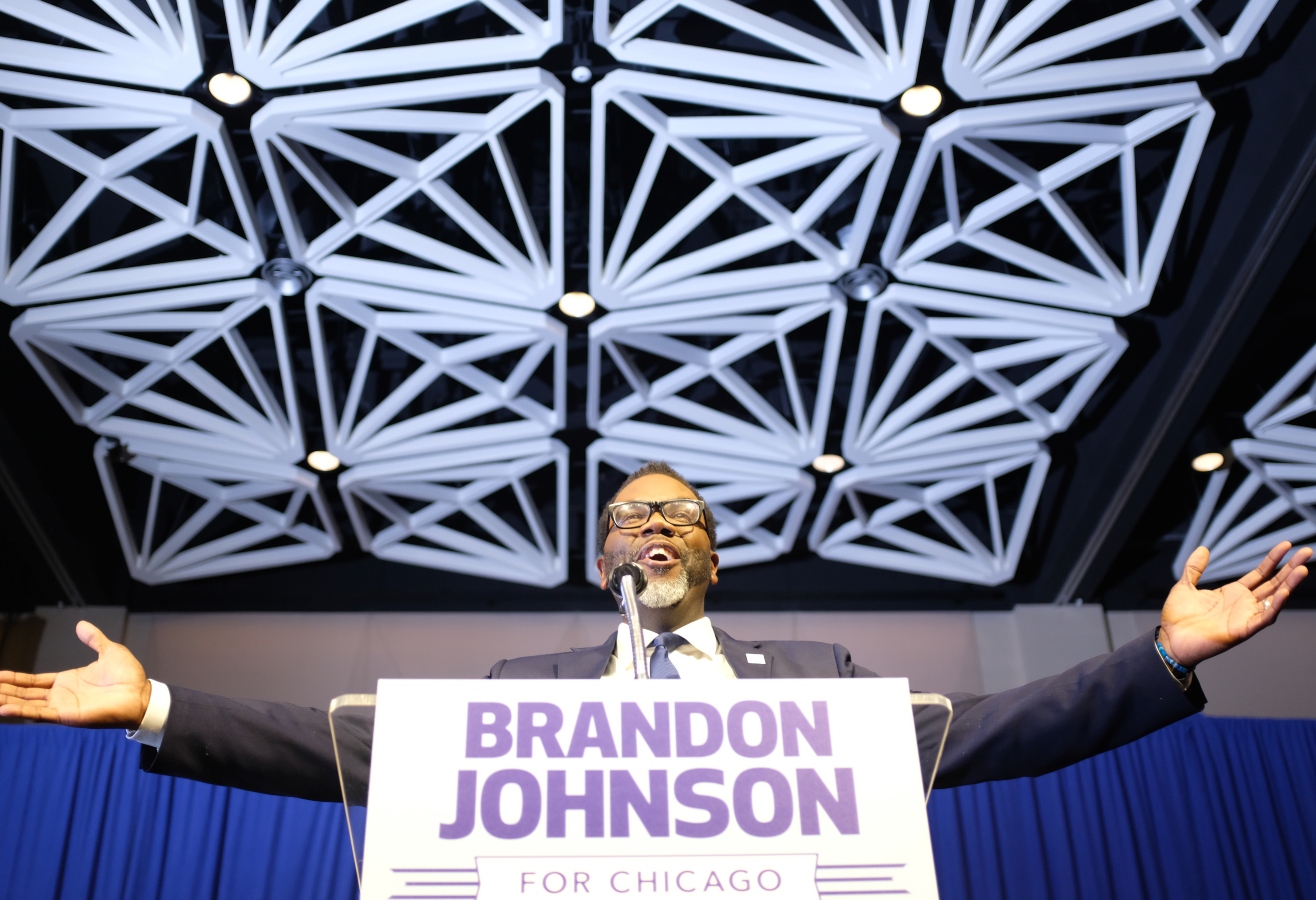 a man with a big smile on his face extends his arms over a sign that says Brandon Johnson