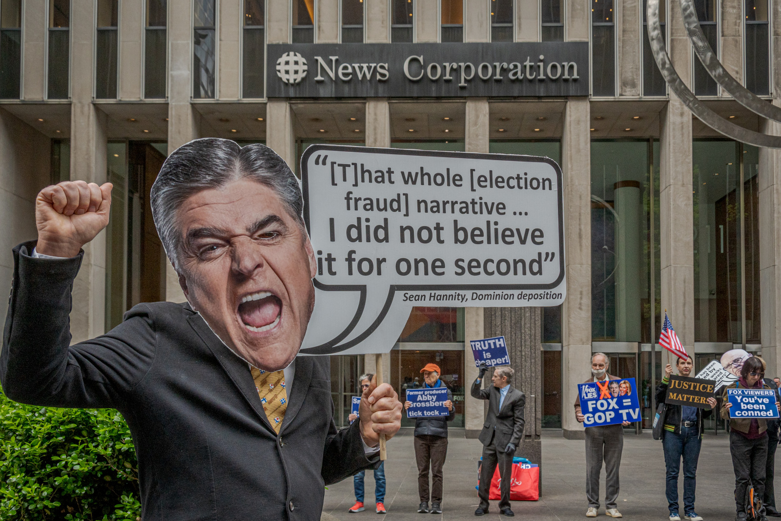 Photo of a protester holding a sign with Sean Hannity's head and the quote "That whole election fraud narrative... I did not believe it for one second"