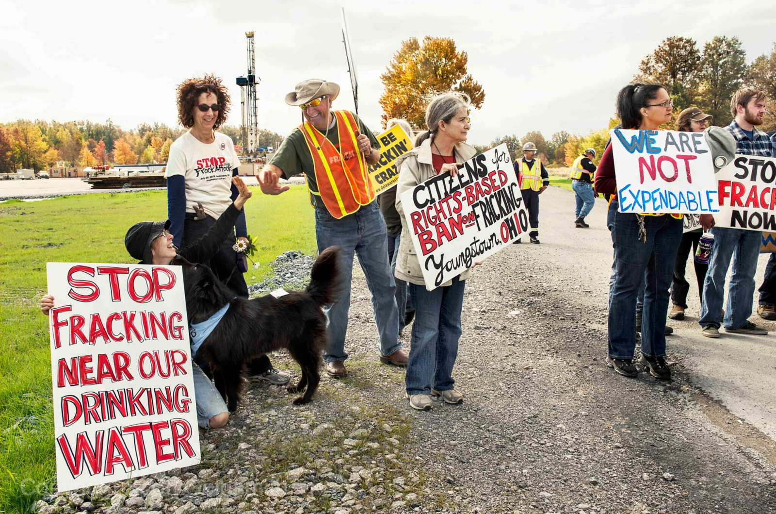 A group of people with signs and a dog protest fracking.