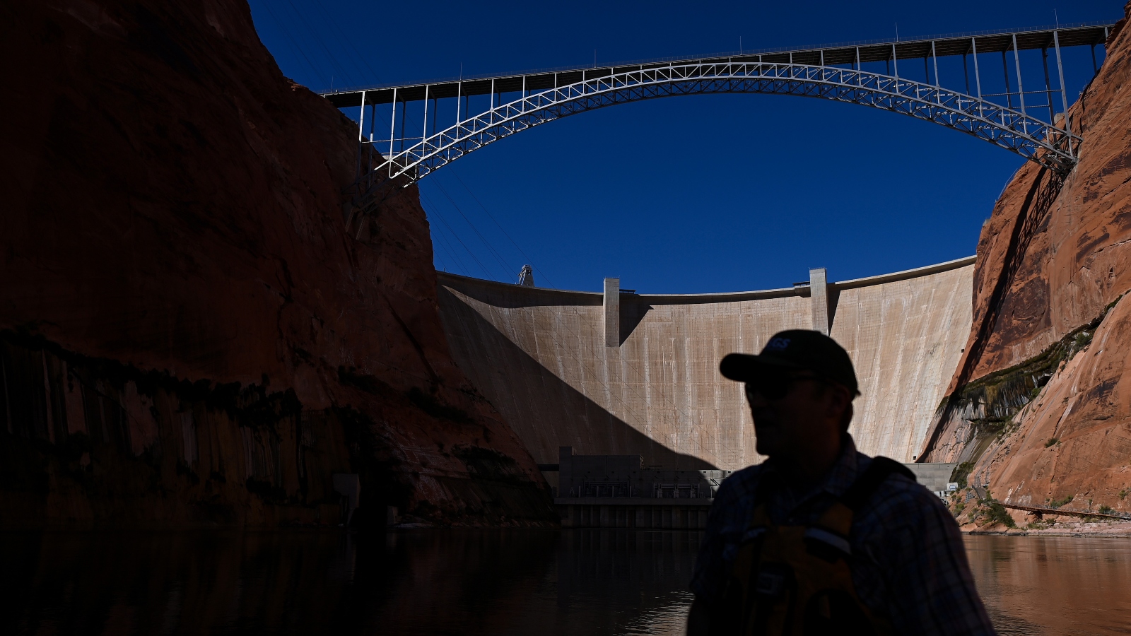 Research ecologist Ted Kennedy drives his boat along the Colorado River as the Glen Canyon Dam is seen in the background.
