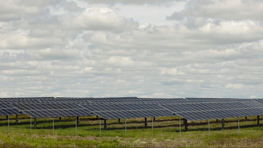 A green field covered in black solar panels under a cloudy sky.
