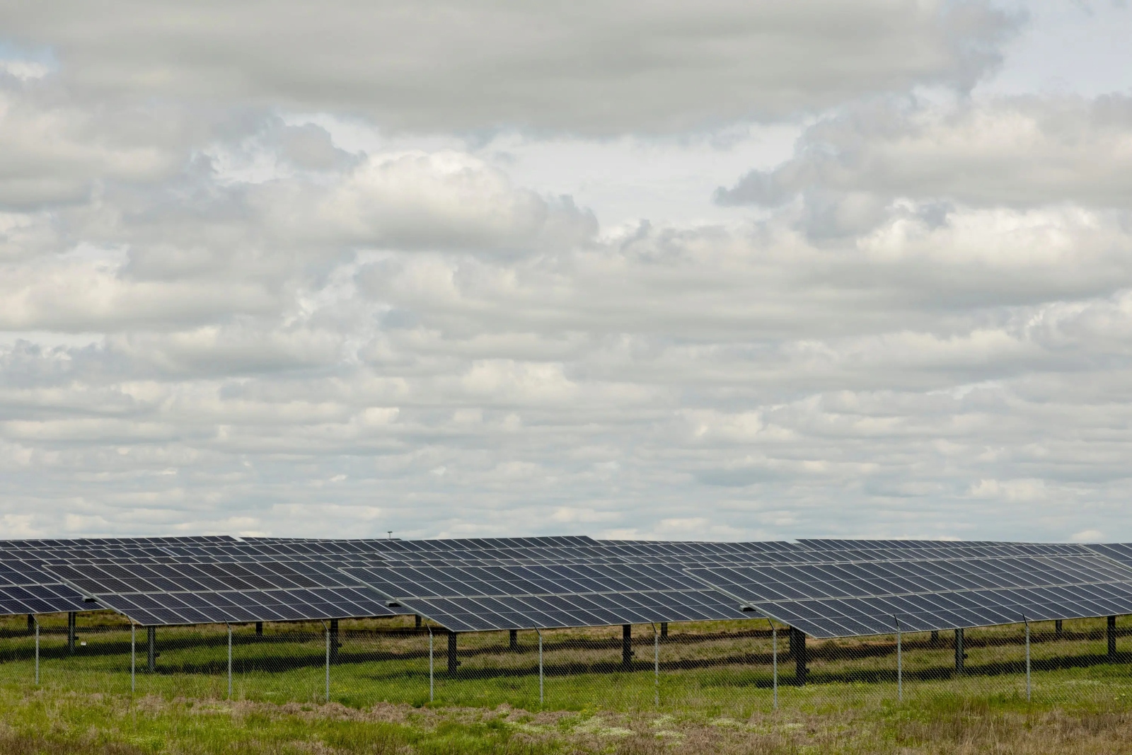 A green field covered in black solar panels under a cloudy sky.