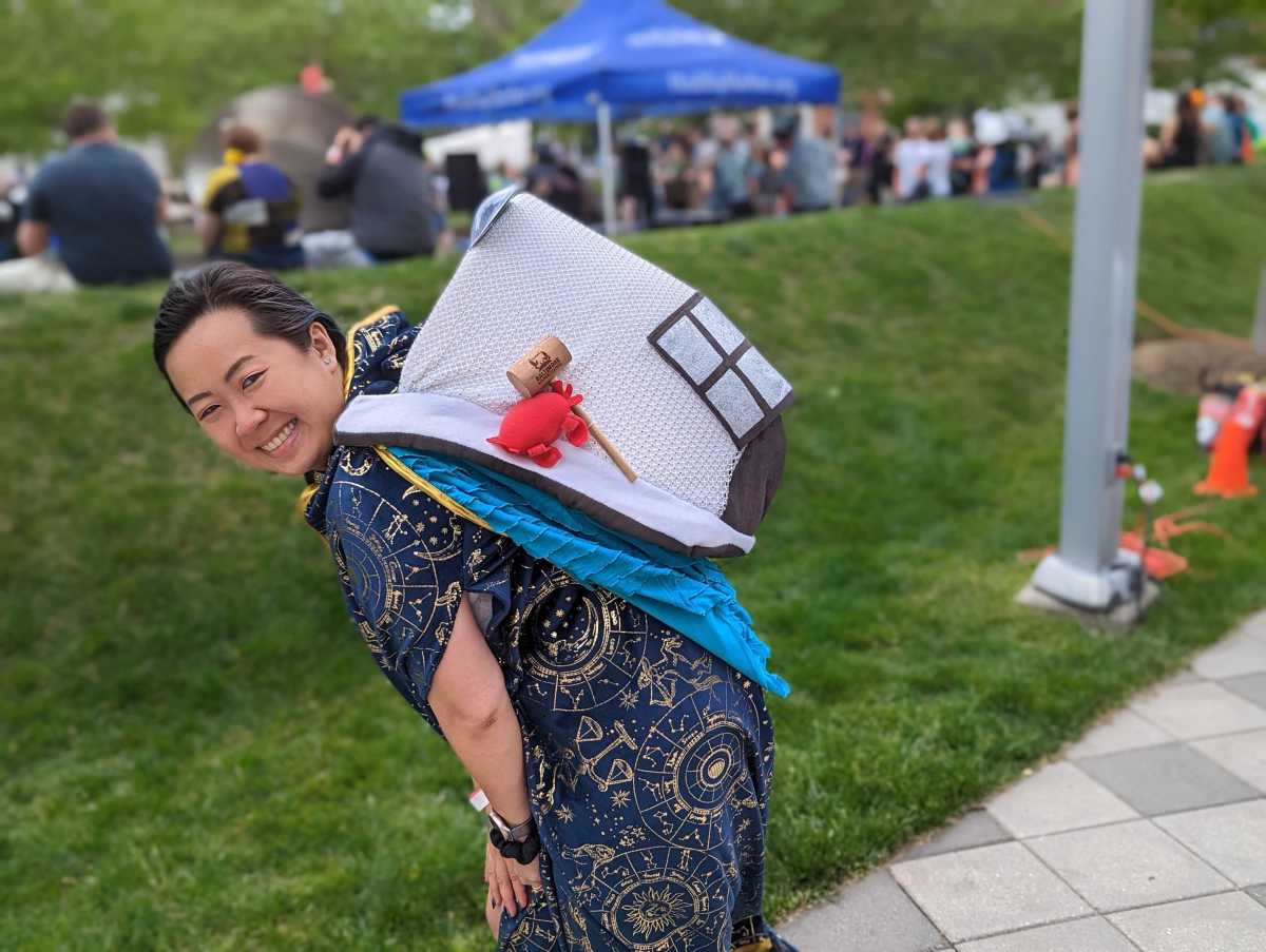 A young smiling Asian woman shows off the trash wheel backpack she is wearing.