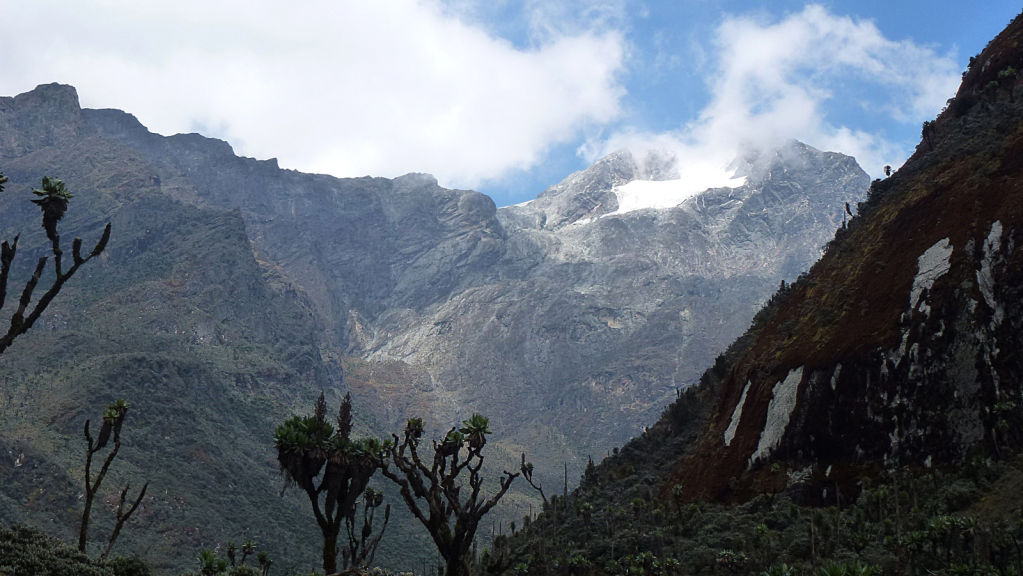 Over the slope of a green mountain, a snow-covered mountain peak appears in the distance.
