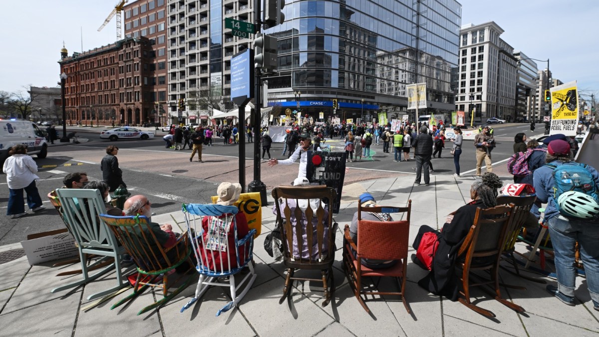 Protestors sitting in colorful rocking chairs on a busy city sidewalk.