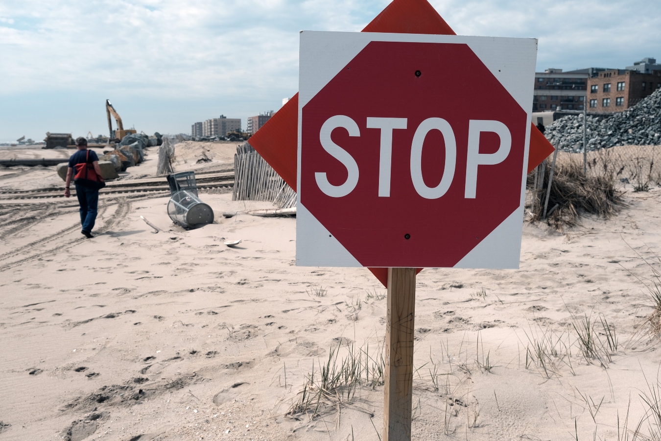 A stop sign is posted on a beach filled with construction equipment.