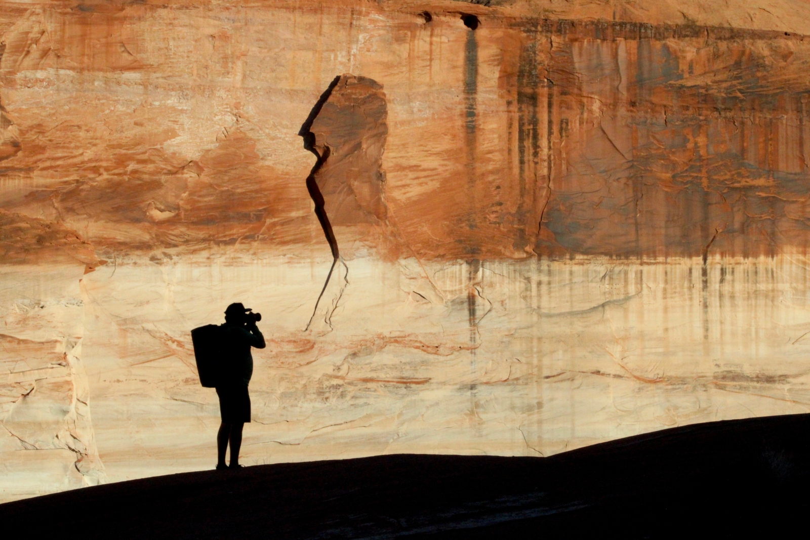The silhouette of a man with a backpack and camera is reflected on a red and cream-colored wall.