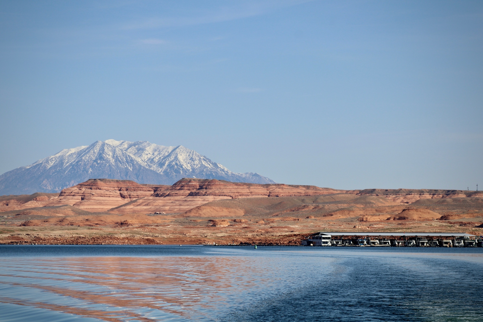 A snow-capped mountain rises behind red rock mesas and a lake.