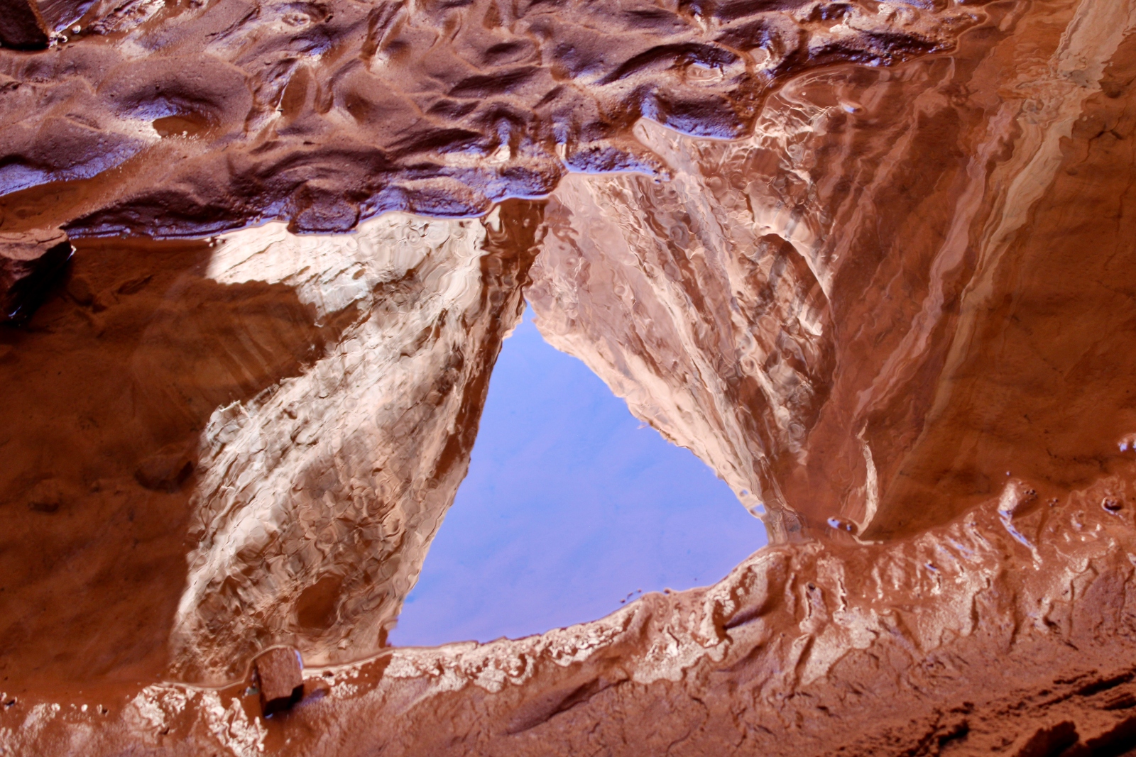 A pool of water in red mud reflects the red canyon walls above.