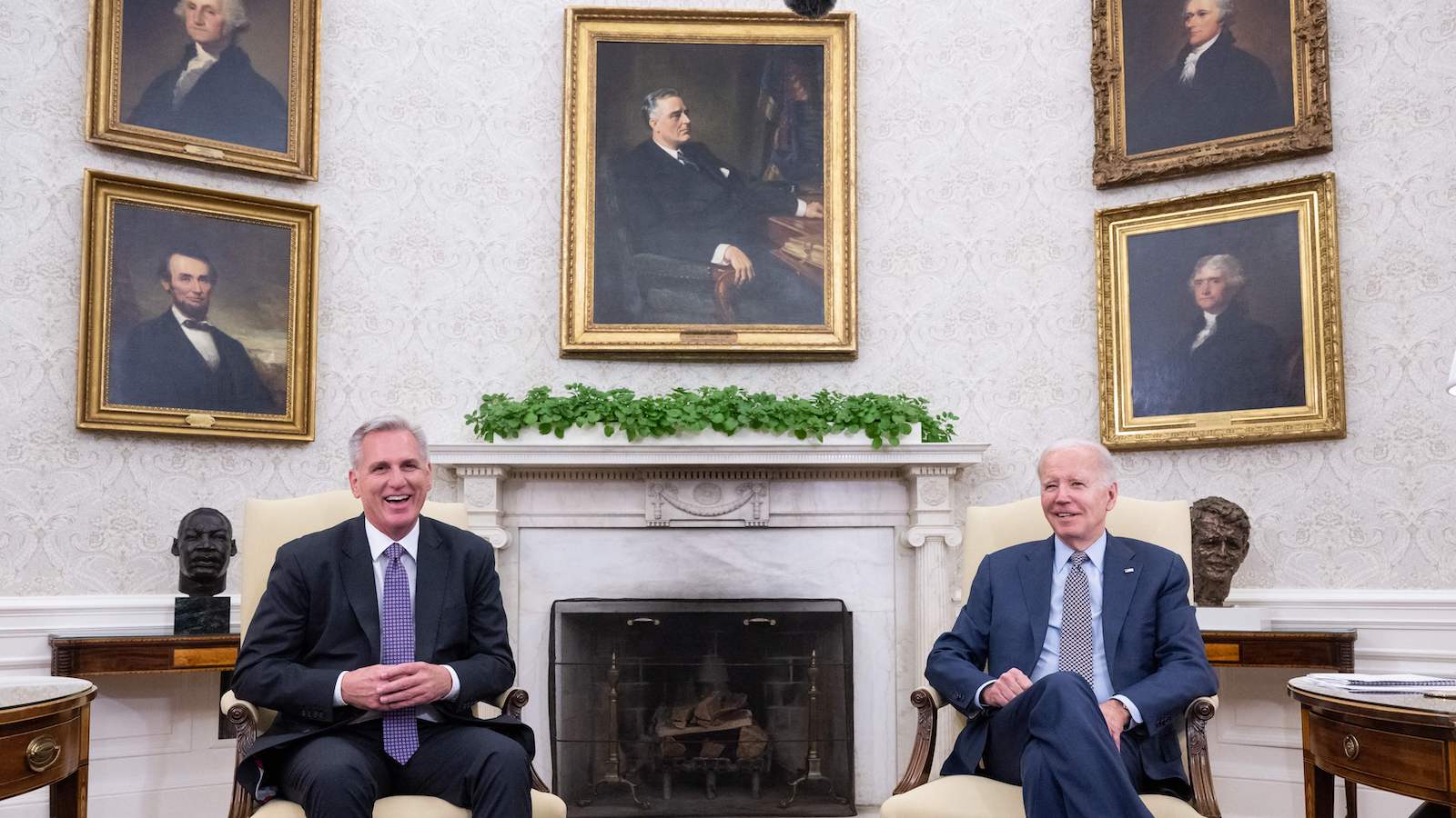 McCarthy and Biden seated with portraits in the background