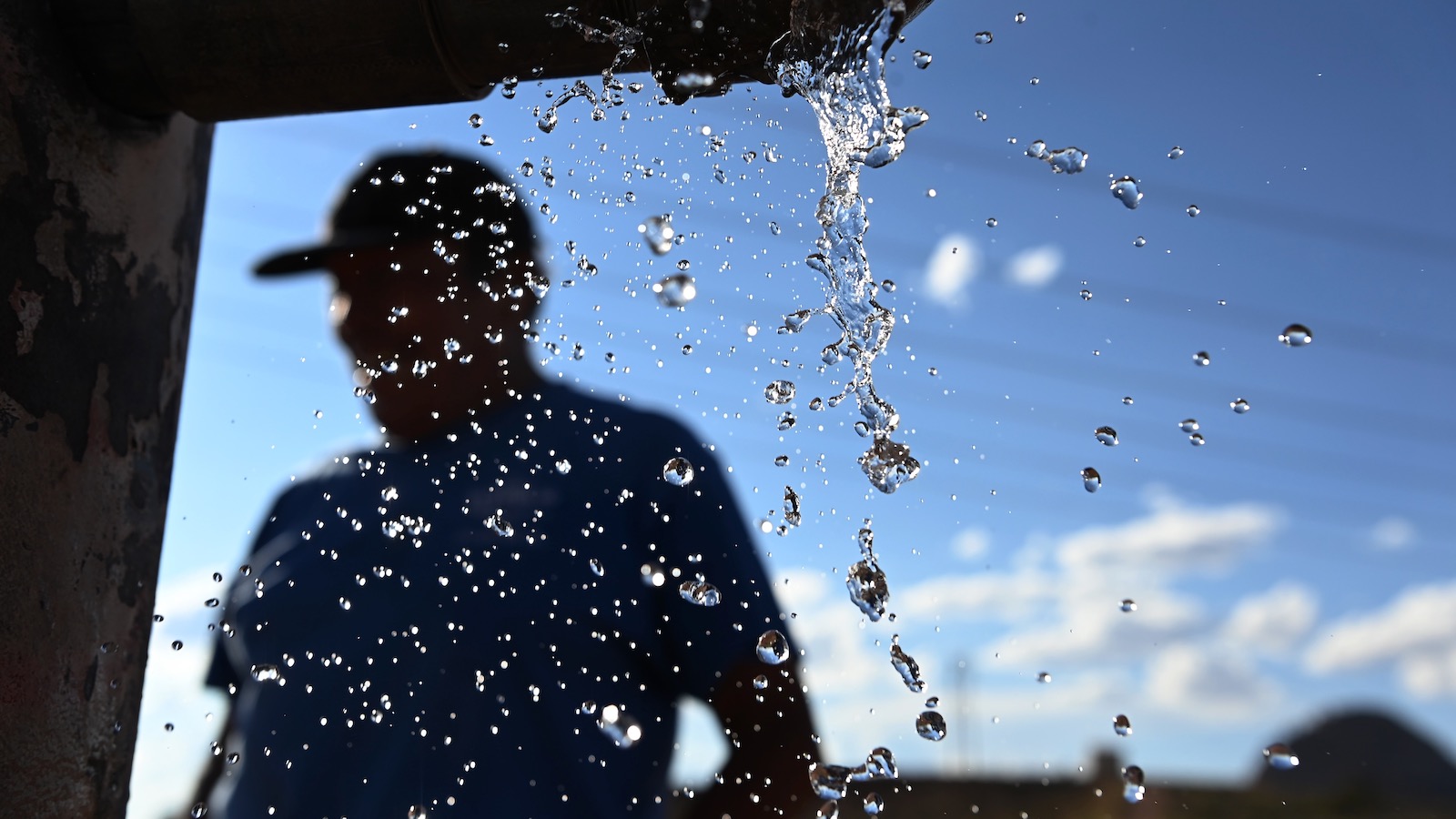 A Navajo man, shown in silhouette, fills a water tank in the back of his truck.