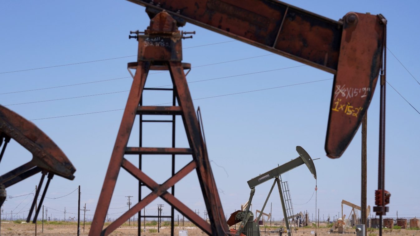 A large metal structure, known as a pumpjack, swings its mechanical arm to the earth for oil production.