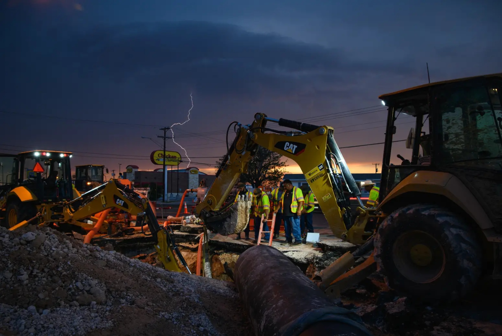 Lighting strikes as heavy machinery digs up a street under a dark stormy sky.