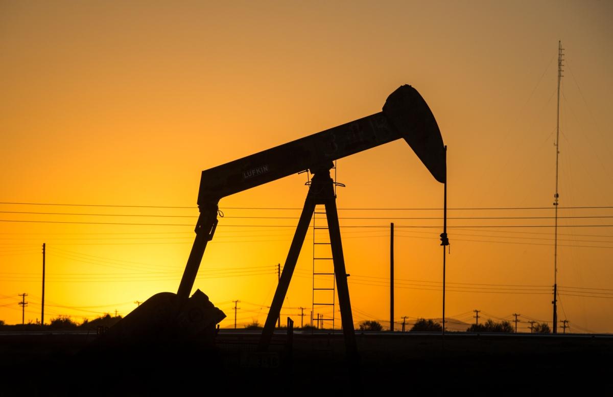 A piece of huge oil machinery is silhouetted against an orange sky with the sun just about to rise.