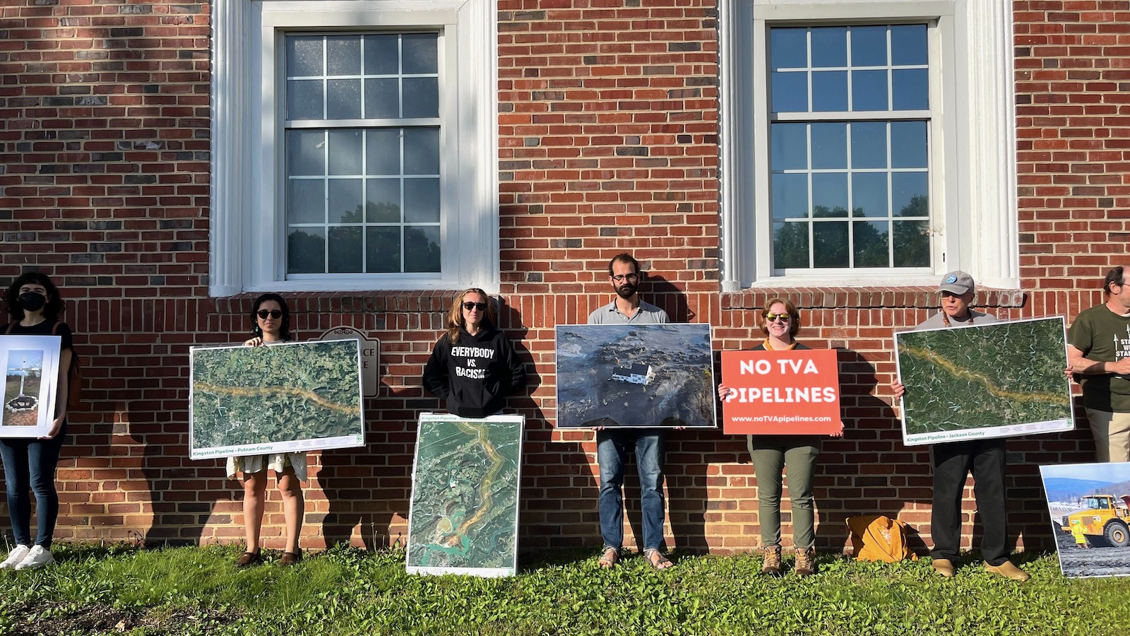 Seven people holding protest signs in front of the brick wall of a building during a demonstration against a proposal by the Tennessee Valley Authority to build two natural gas power plants.