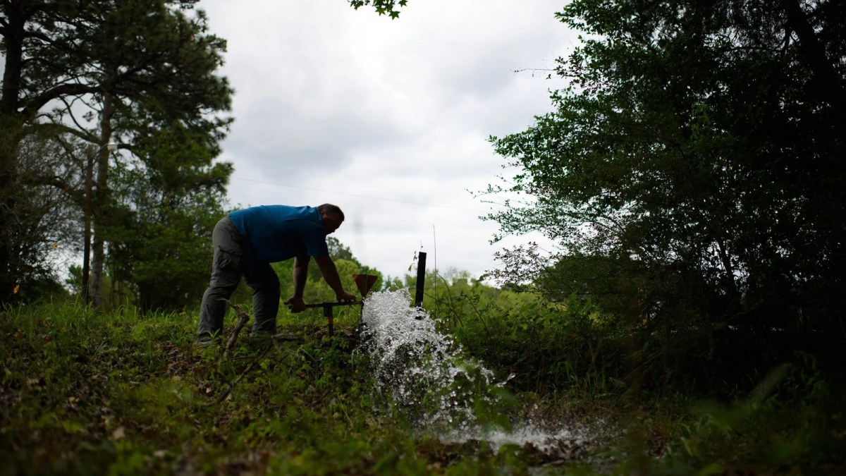 A man stands on a hill under a cloudy sky as water pours from a pipe.