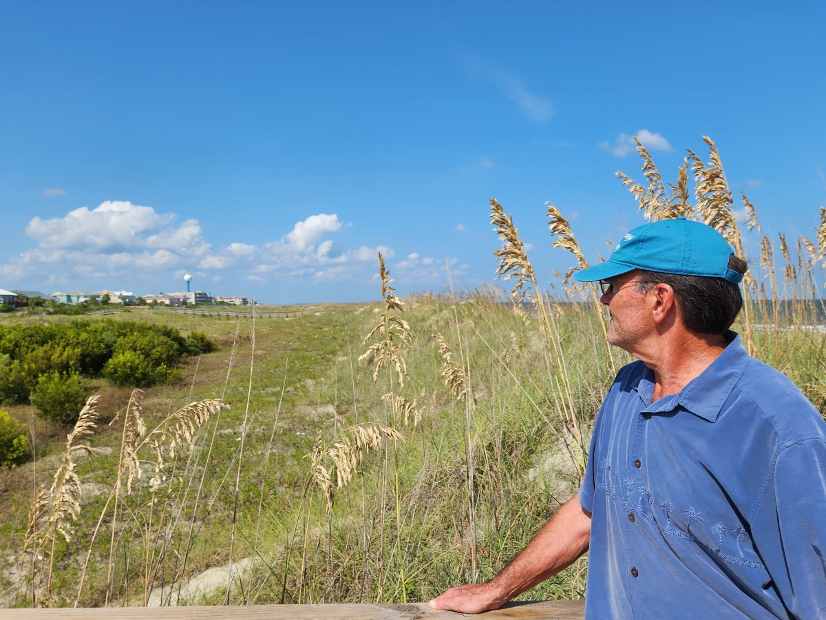 A man in a blue shirt with a blue cap looks out over the swampy area.