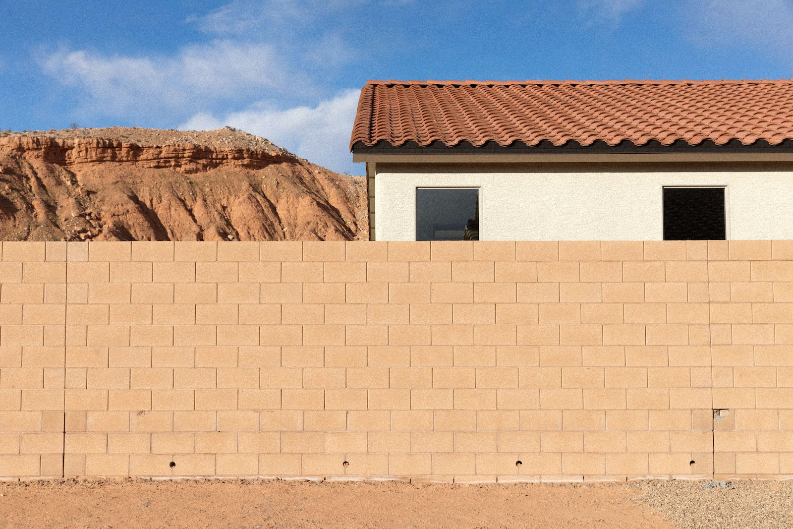 a sandy brick wall near a house and mountains