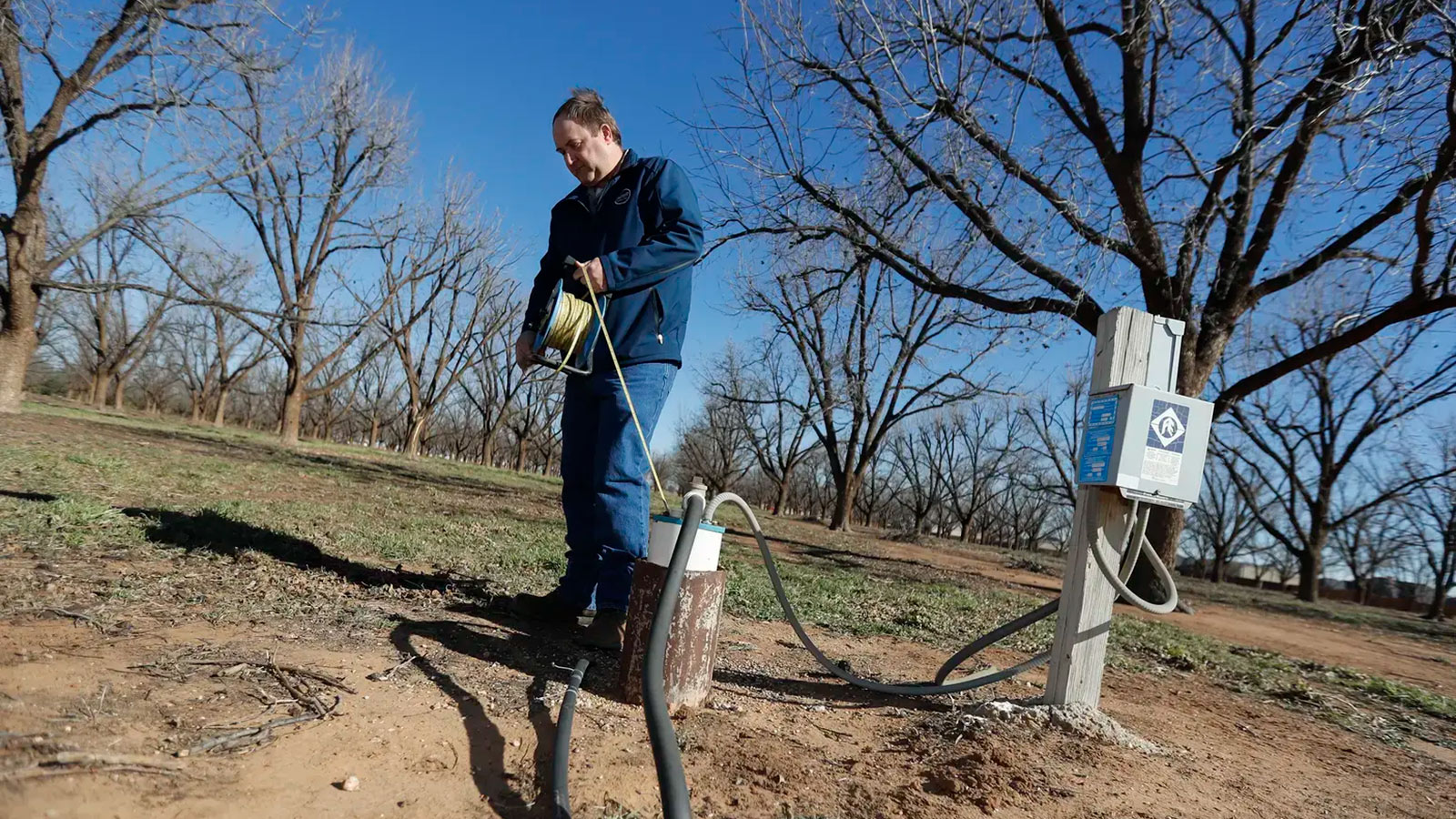A man unrolls a rope attached to a metal cylinder in the ground.