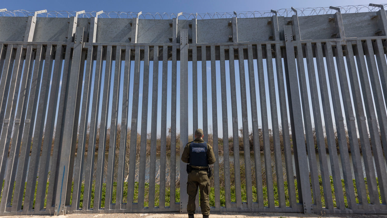 Photo of a border patrol office standing in front of a tall fence.