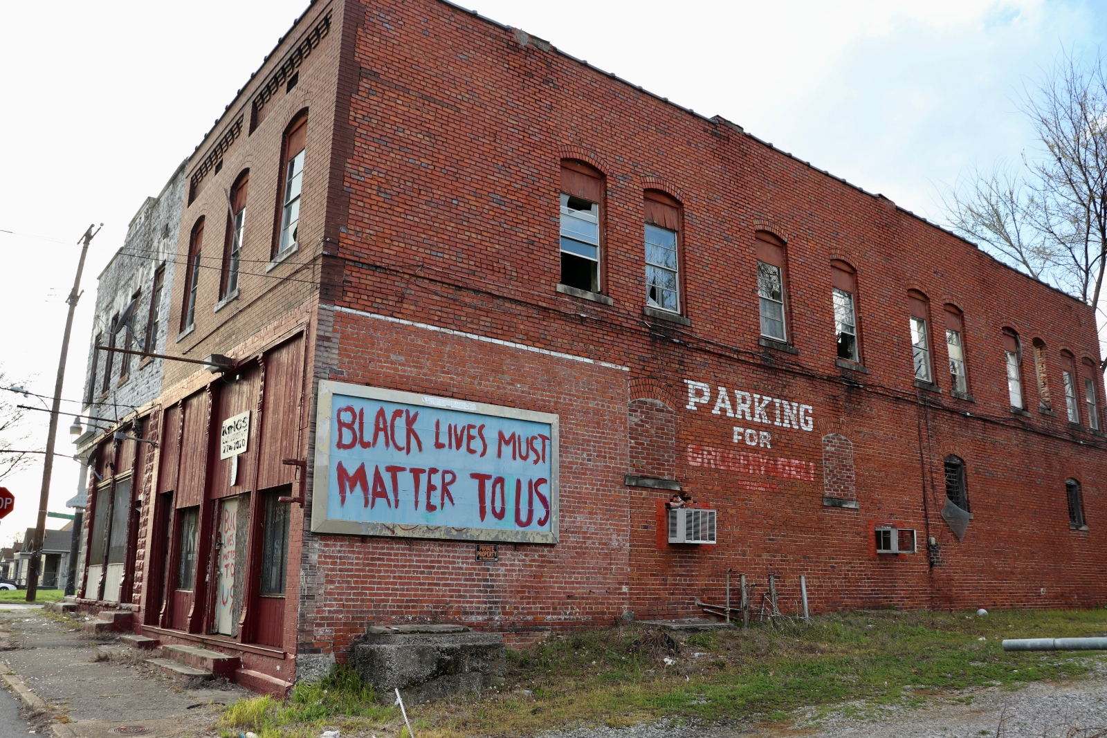 A red brick building has a spray-painted sign that says Black Lives Must Matter to Us