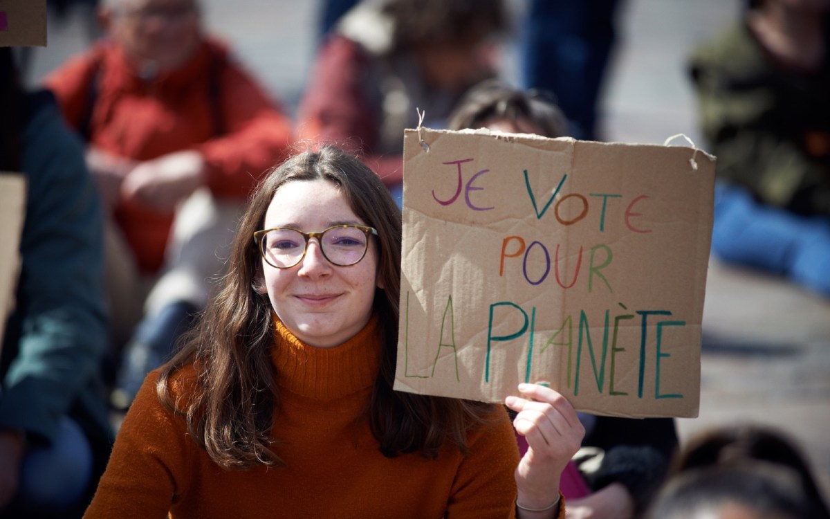 A young woman holds up a cardboard sign reading "Je vote pour la planète"