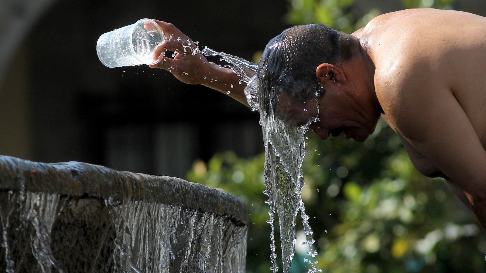 A man leans over a fountain in a park to pour a cup of cold water over his head as a heat wave grips Guadalajara, Mexico