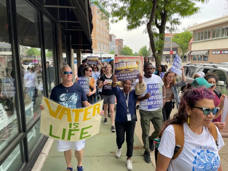 A group of people with "water is life" signs march down a city street.