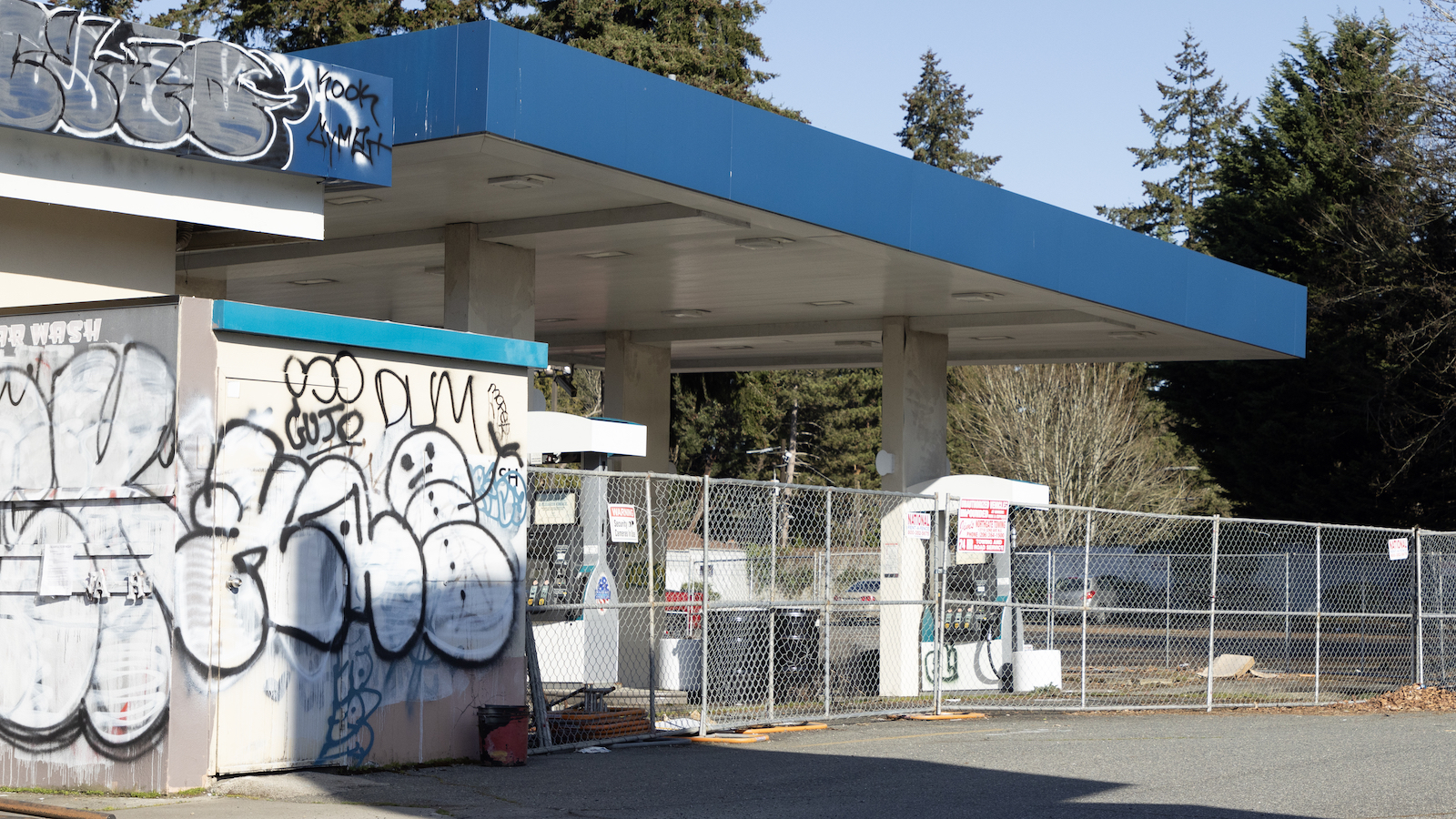 a gas station with a blue awning and chain link fence.
