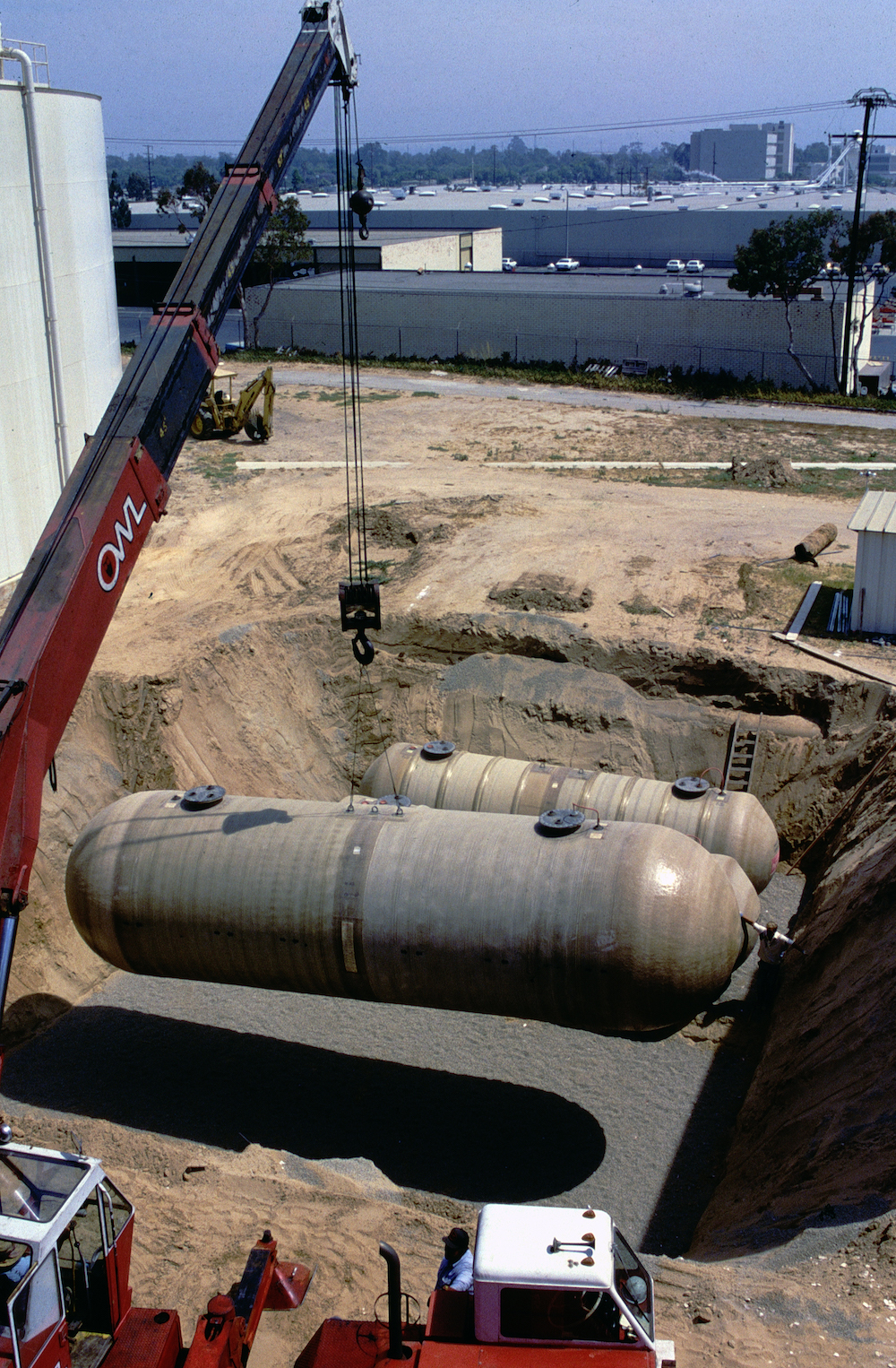 a large cylinder gas storage tank is lowered into a pit by a crane