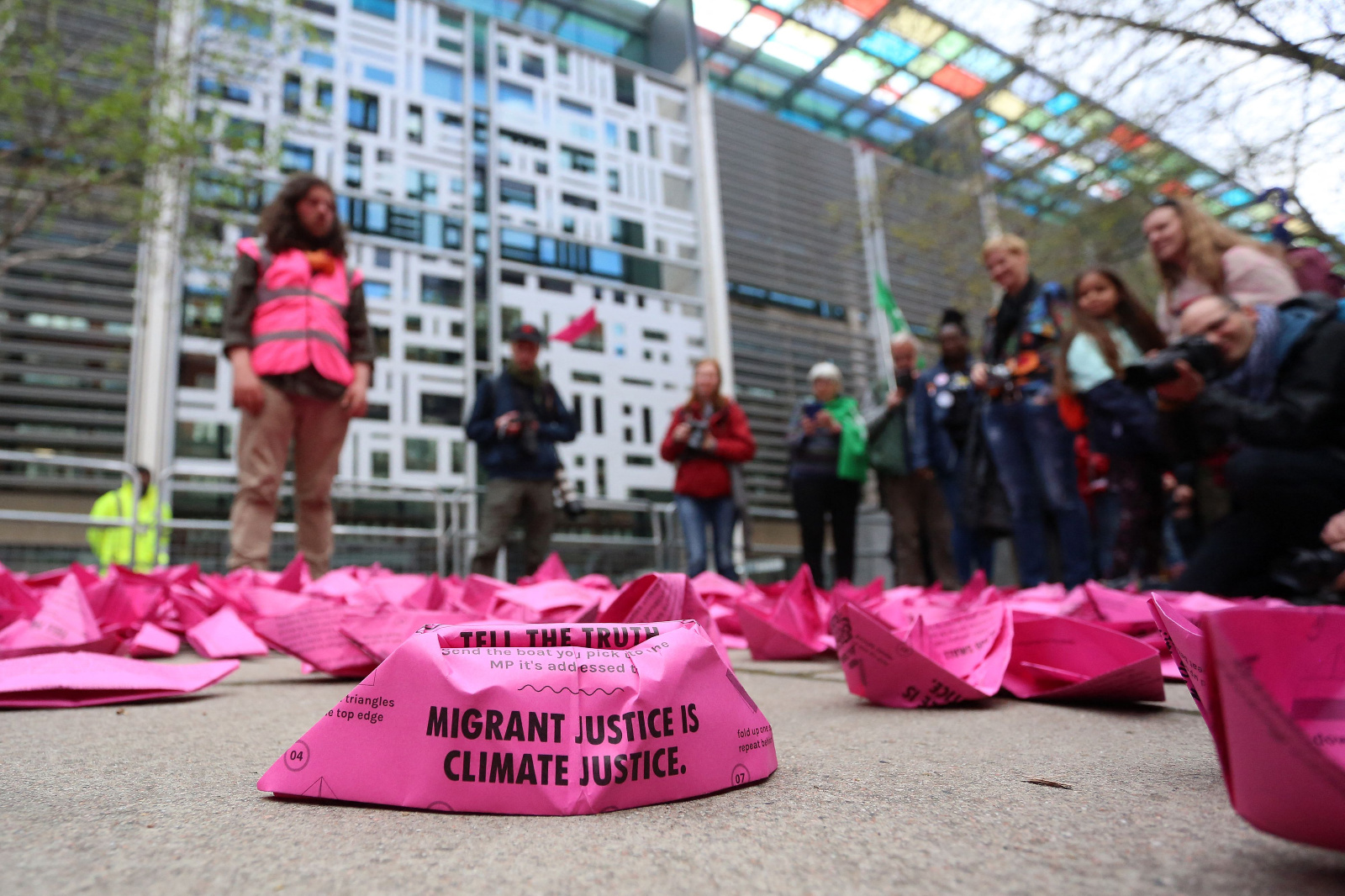 A pink, boat-shaped item at a protest says "migrant justice is climate justice."
